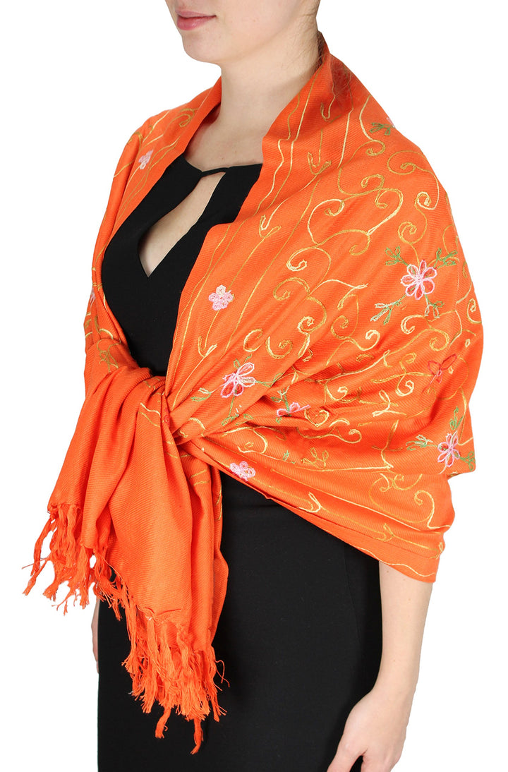 Hand-embroidered floral patterns on a soft orange pashmina shawl with decorative fringe edges