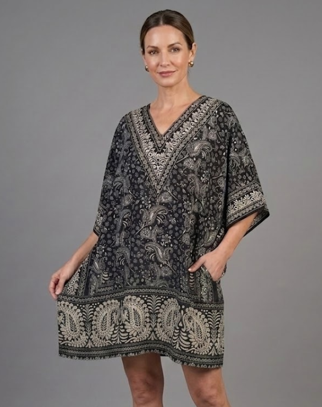 Woman modeling a black and silver paisley print V-neck kaftan dress with short sleeves and side pockets, luxury bohemian resort wear.