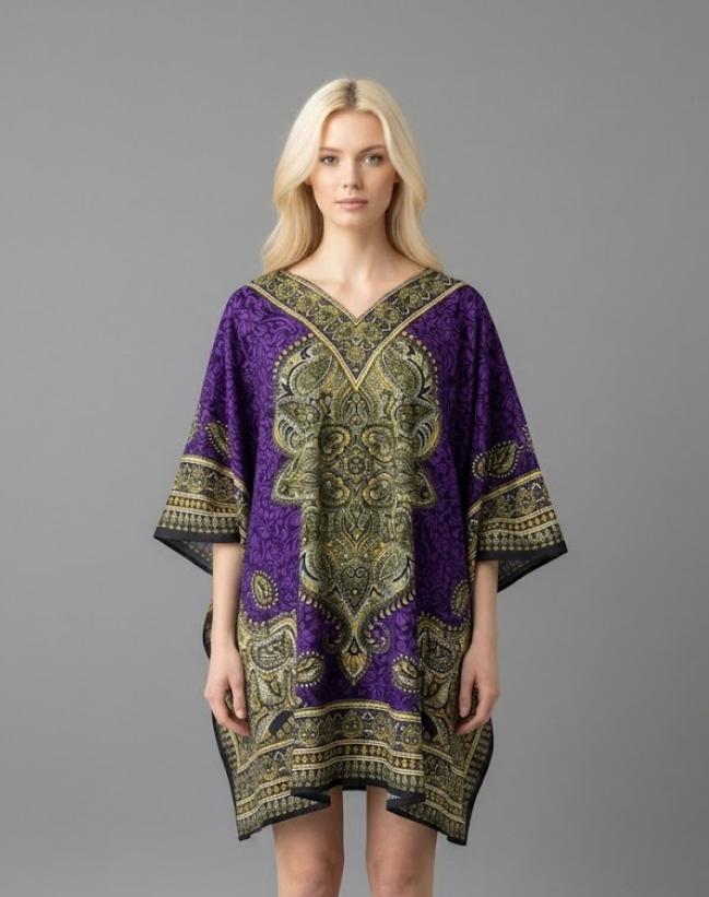 Woman modeling a vibrant royal purple kaftan tunic with a large, ornate olive and gold paisley medallion print. The short, one-size V-neck dress features a decorative border and draped sleeves, shown against a solid grey background.