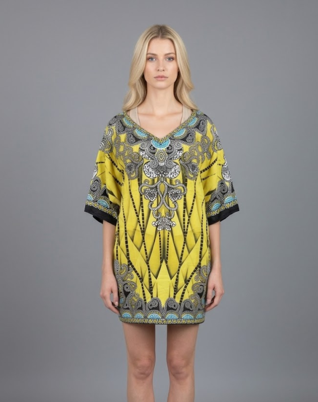 Woman modeling a bright lemon yellow kaftan tunic featuring a modern geometric abstract pattern and intricate silver-grey ornate medallion details at the neckline. The short, one-size V-neck dress is shown against a solid grey background, perfect for vibrant resort fashion.